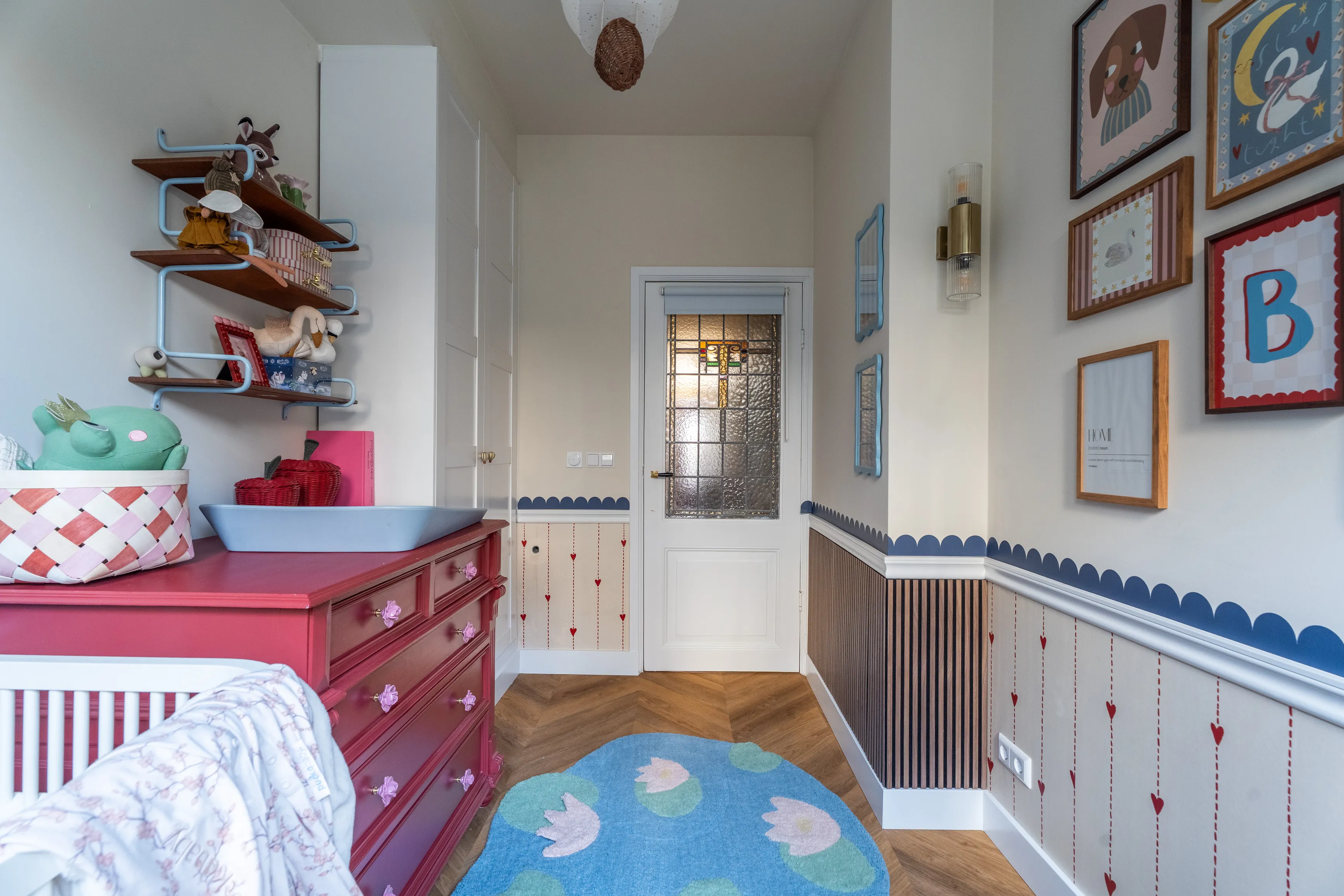 A lily pad rug and berry red dresser beneath scalloped blue trim and a stained glass door