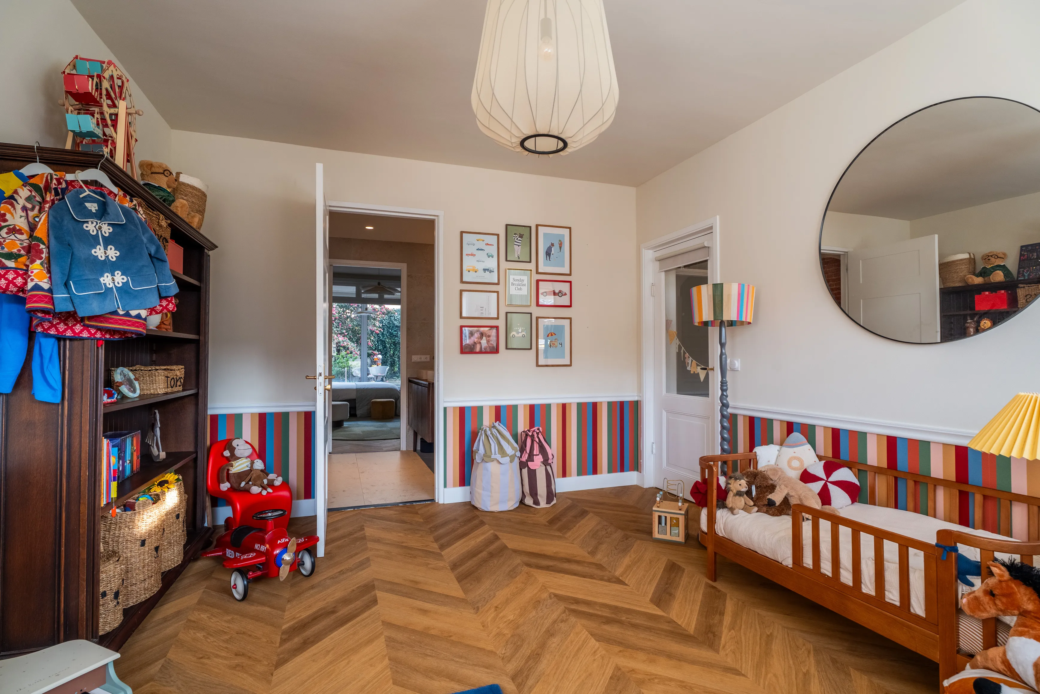 A wooden toddler bed beside a gallery wall, a red scooter on a herringbone floor