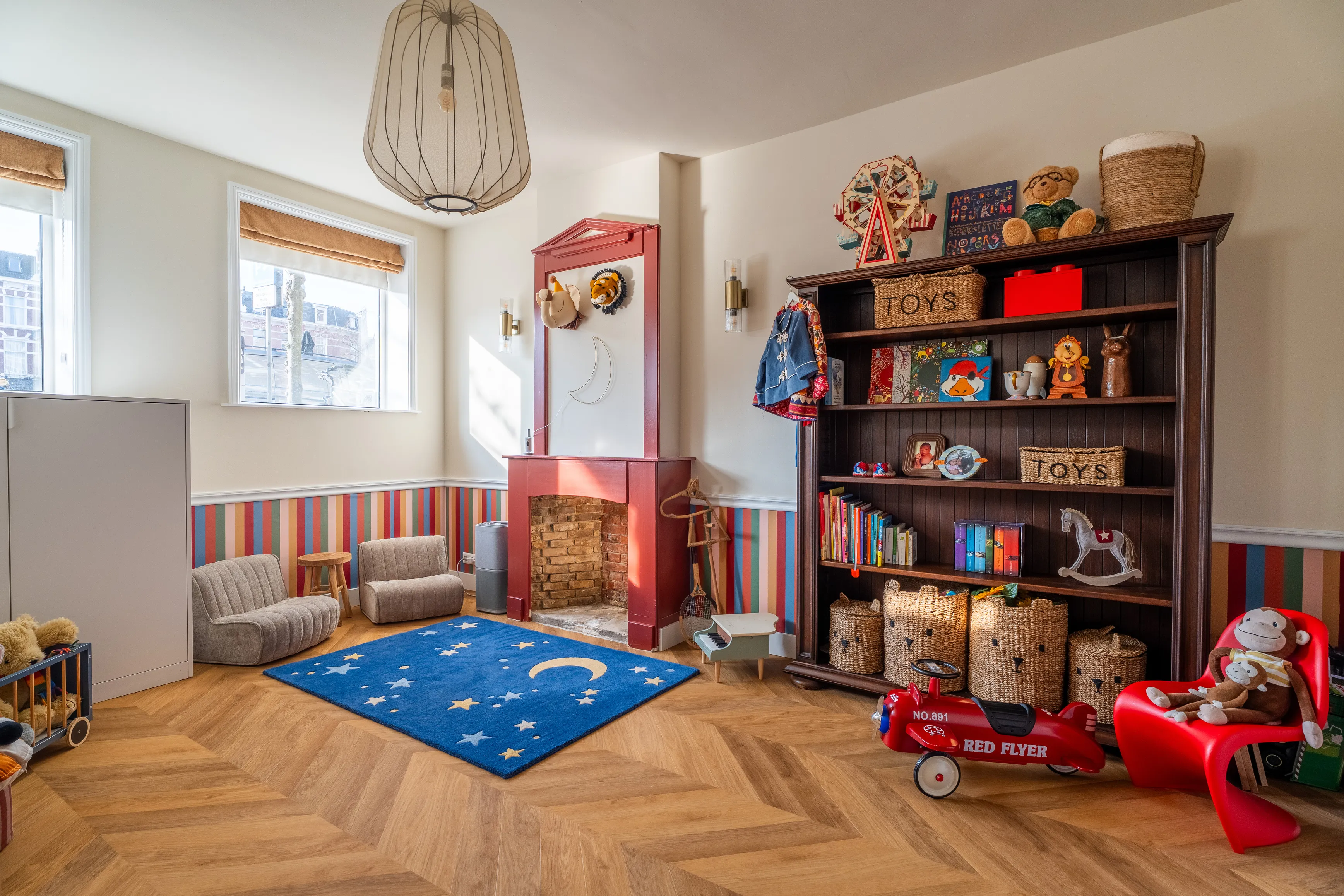 The Carousel Room, a warm playroom with striped walls, a red painted fireplace and a bookshelf full of toys